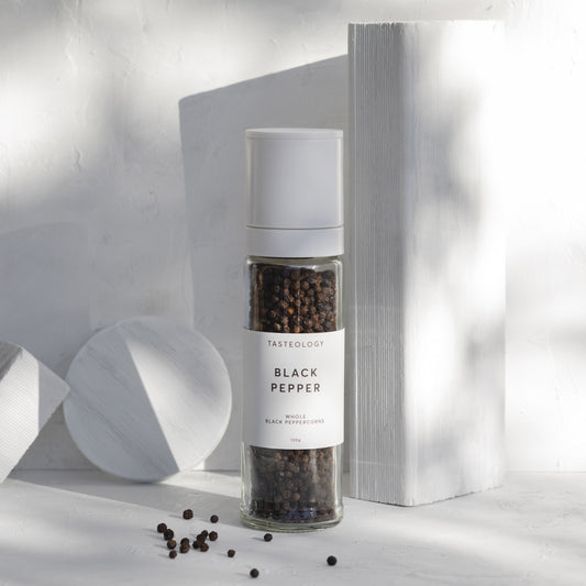 Black pepper grinder with white lid place in front of white marble