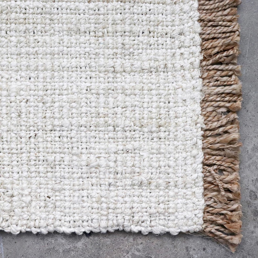 Close up of white woven floor mat with straw coloured fringe detailing